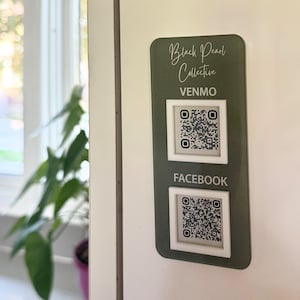 May include: A green sign with white text that reads "Black Pearl Collective" and has two QR codes. The top QR code is labeled "Venmo" and the bottom QR code is labeled "Facebook".