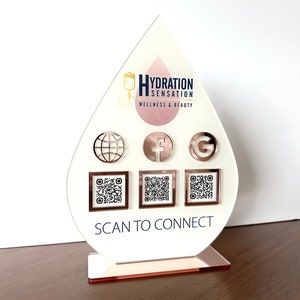May include: A white teardrop-shaped acrylic sign with a gold logo that says "Hydration Sensation Wellness & Beauty". The sign has a globe, Facebook, and Google icons, and three QR codes with the text "Scan to Connect" below.