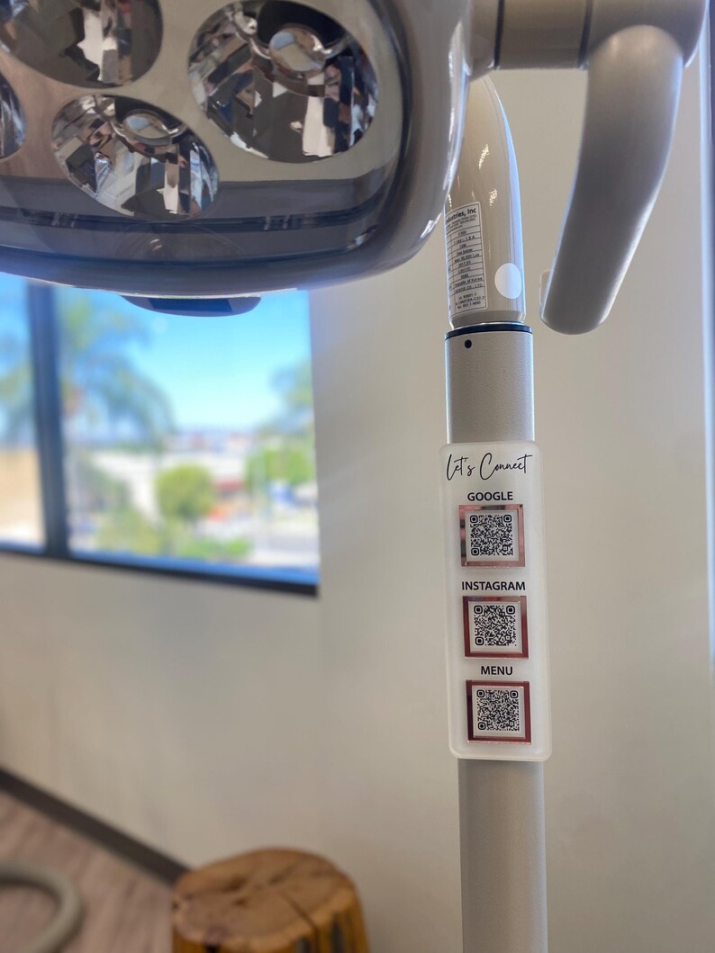 May include: A white dental light with a sticker that says "Let's Connect" and has QR codes for Google, Instagram, and a menu.