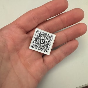 May include: A white square sticker with a black QR code and the letter "V" in the center.