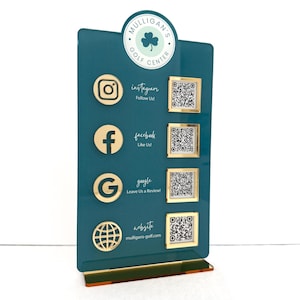 May include: A teal blue sign with a gold border and a gold shamrock logo that says "Mulligan's Golf Center". The sign has four gold icons with QR codes for Instagram, Facebook, Google, and a website.