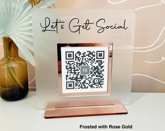 Puede incluir: Un letrero de acrílico esmerilado con una base de oro rosa. El letrero dice "Let's Get Social" y presenta un código QR.