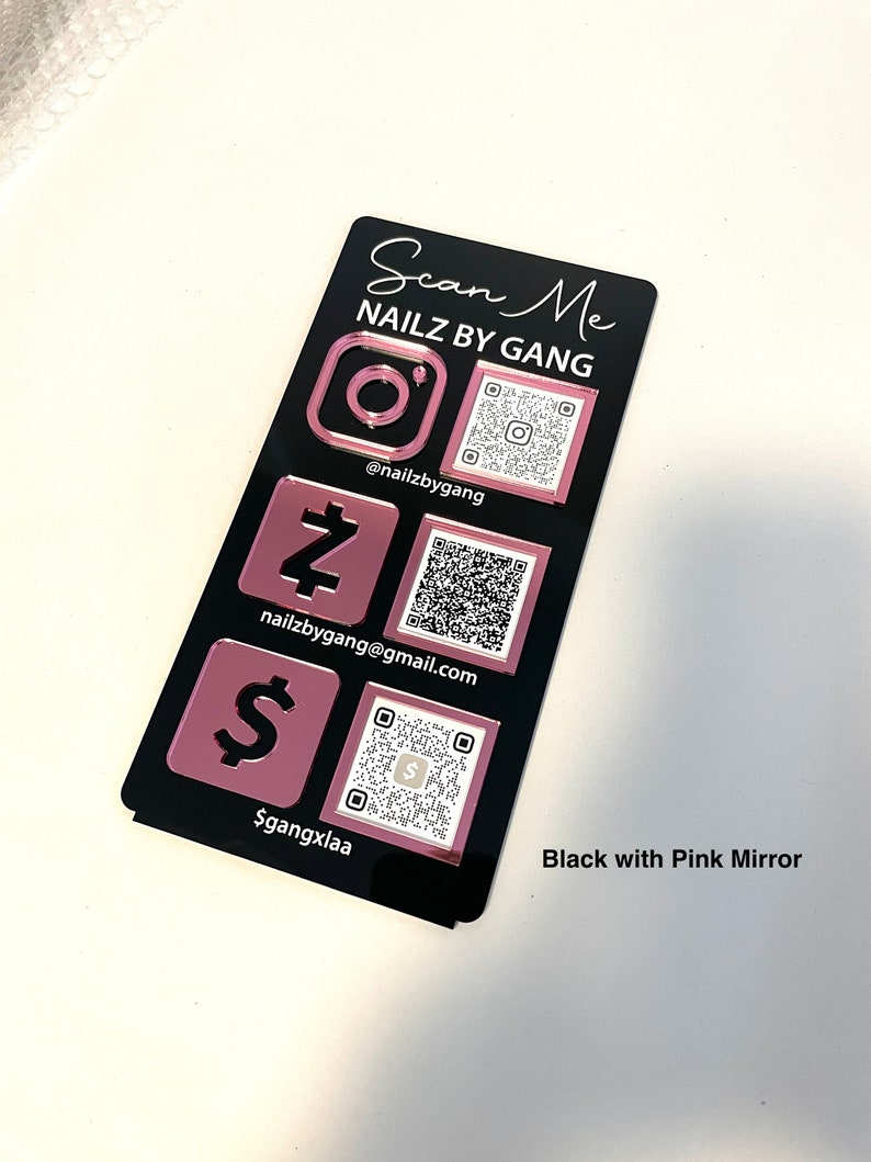 Op de afbeelding: Zwarte acryl visitekaartje met roze spiegelaccenten. De kaart heeft een QR-code, Instagram en andere sociale media-iconen. De tekst op de kaart luidt "Scan Me", "Nailz by Gang", "@nailzbygang", "nailzbygang@gmail.com", "$gangxlaa" en "Zwart met roze spiegel".