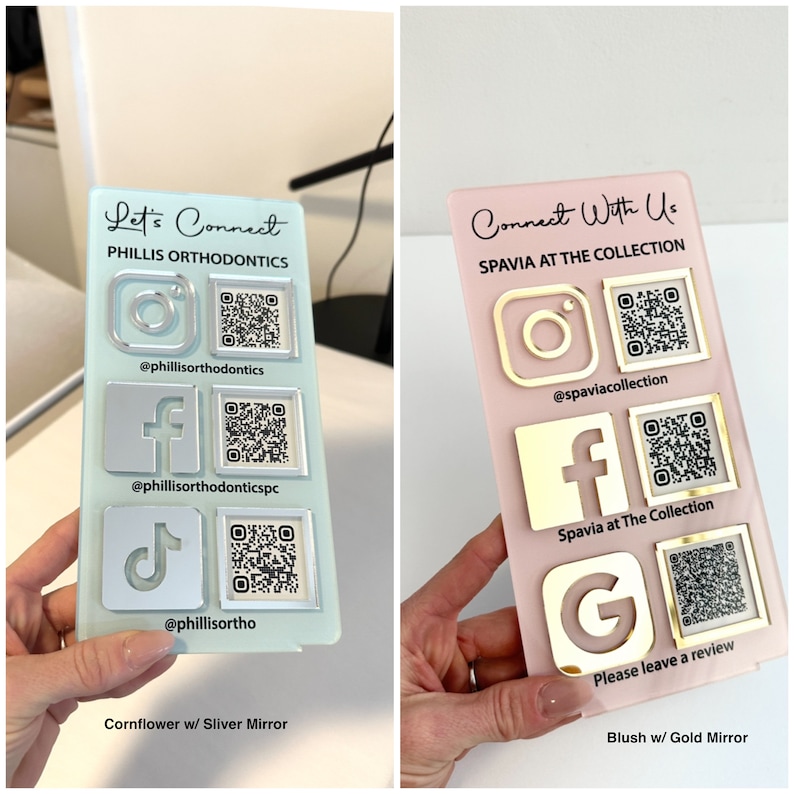 Op de afbeelding: Twee acrylplaten met social media-iconen en QR-codes. De plaat links is lichtblauw met zilveren iconen en de tekst "Let's Connect" en "PHILLIS ORTHODONTICS". De plaat rechts is roze met gouden iconen en de tekst "Connect With Us" en "SPAVIA AT THE COLLECTION".
