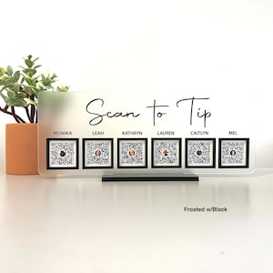 May include: Frosted acrylic sign with the text "Scan to Tip" and six QR codes labeled with names: Monika, Leah, Kathryn, Lauren, Caitlyn, and Mel. The sign is on a black stand.