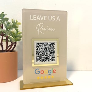 May include: Champagne-colored acrylic sign with a gold frame and white text that says "LEAVE US A Review". The sign has a QR code and the Google logo with stars.