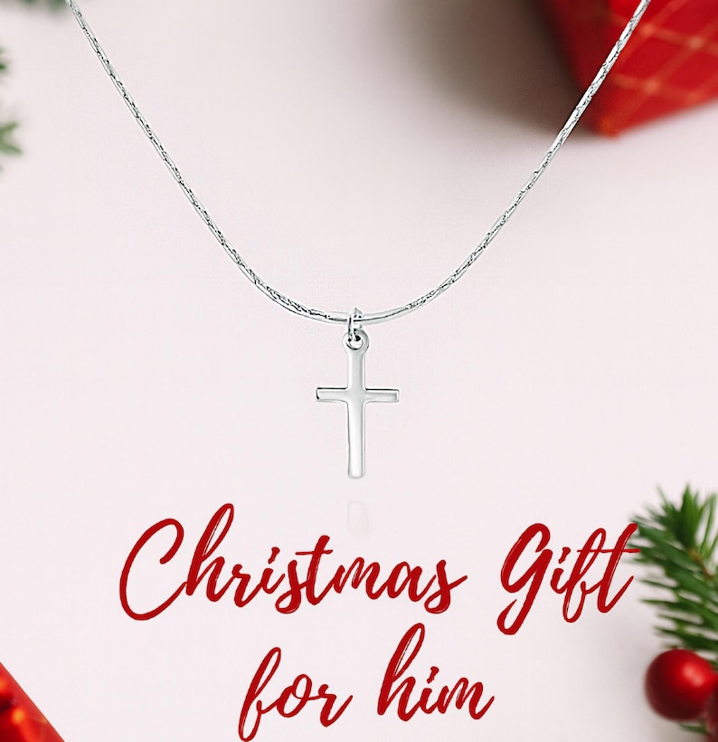 May include: A silver-toned chain necklace featuring a simple, smooth cross pendant. The text "Christmas Gift for him" is printed in red script below the pendant. The necklace is displayed against a light background with red and green accents.