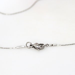 May include: A silver-toned metal necklace chain featuring a lobster claw clasp mechanism. The chain consists of small, interconnected links that extend from both sides of the central fastening hardware, which is secured by a circular jump ring.