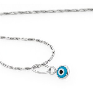 May include: A silver-toned chain necklace featuring a small, circular pendant with an evil eye motif. The pendant displays a central black pupil surrounded by a light blue iris and a white outer ring, all encased in a smooth, polished silver-toned metal frame.