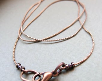 May include: A thin copper-toned chain necklace featuring a textured, rope-like link design. The necklace includes a lobster claw clasp and a circular jump ring, both finished in a matching copper tone, with small dark beads near the closure.