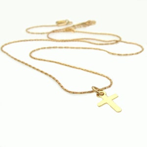 May include: A gold-toned metal necklace featuring a simple, plain cross pendant suspended from a delicate, textured chain. The cross has smooth, flat surfaces and rounded edges, while the chain consists of small, interconnected links.