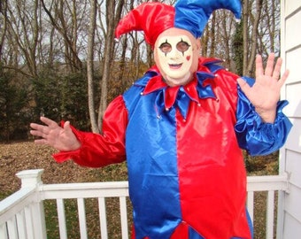May include: A jester costume with a red and blue satin fabric. The costume features a pointed hat with bells and a mask with a painted smile.