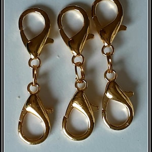 May include: Three gold-toned metal lobster claw clasps with a swivel hook on each. The clasps are attached to a chain.