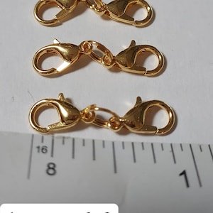 May include: A set of three gold-toned lobster claw clasps, each measuring approximately 1 inch in length. The clasps are shown against a white background with a ruler for scale.