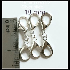 May include: Set of three silver-colored, 18 mm lobster claw clasps. The clasps are connected by small chains. A ruler shows the clasps are approximately 0.7 inches in length. Text in the image reads "18 mm set of 3" and "Silver pltee."