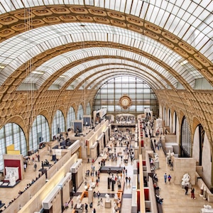 May include: An overhead view of a large, ornate museum interior with a glass ceiling. The museum is filled with people and exhibits, and the walls are decorated with intricate carvings. The museum has a large clock on the wall.