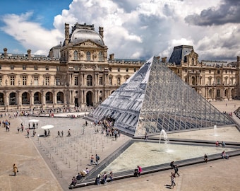 May include: An aerial view of the Louvre Museum in Paris, France. The iconic glass pyramid stands in front of the museum, surrounded by a courtyard with fountains and people walking around.