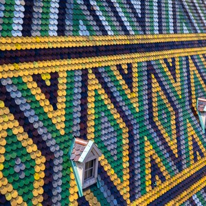 May include: A close-up of a colorful tiled roof with a geometric pattern. The tiles are arranged in a repeating pattern of green, yellow, and blue. There are two small windows in the roof.