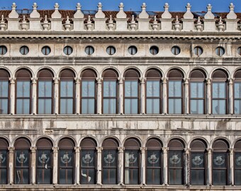 May include: A white building with a row of arched windows. The windows have brown wooden frames and are divided into multiple panes. The building has a decorative cornice with small spires.