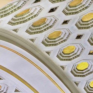 May include: Architectural detail of a curved ceiling with a repeating pattern of octagons and diamonds. The ceiling is painted white with gold accents, creating a sense of depth and elegance. The design is symmetrical and ornate.