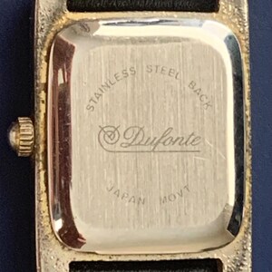 May include: The back of a gold-tone watch with a black leather band. The watch face is engraved with "Stainless Steel Back", "Duforte", and "Japan Movt".