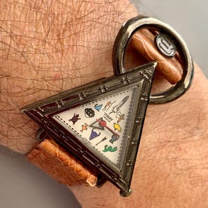 May include: A vintage wristwatch with a triangular face and a brown leather band. The watch face features various colorful icons and the words "TODAY TIME WEAR". The watch is attached to a large, circular silver-toned metal band.