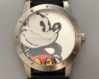 May include: A silver wristwatch with a black leather band features a Mickey Mouse illustration on the face. The watch has silver hands and a white face with black markings.