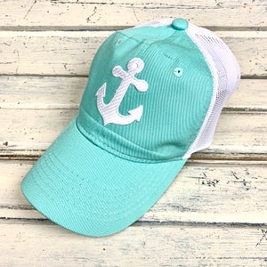 May include: A turquoise and white trucker hat with a white anchor embroidered on the front.