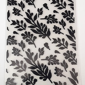 May include: A clear plastic sheet with a black floral pattern. The pattern features various sizes and shapes of leaves and branches.
