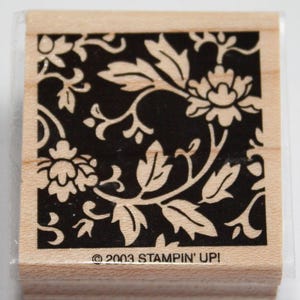 K&ouml;nnte beinhalten: Ein schwarzer und wei&szlig;er Gummistempel mit einem floralen Design. Der Stempel zeigt ein sich wiederholendes Muster aus Bl&auml;ttern und Blumen. Der Text "&copy; 2003 STAMPIN' UPI" ist auf der Unterseite des Stempels aufgedruckt.