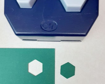 May include: A blue hexagon paper punch with two light gray hexagon-shaped push buttons. The punch is next to a green sheet of paper with two white hexagon cutouts and two green hexagon shapes.