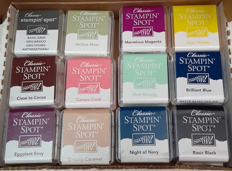 May include: A collection of ten ink pads in various colors, including basic gray, mellow moss, marvelous magenta, yoyo yellow, close to cocoa, cameo coral, mint melody, brilliant blue, eggplant envy, creamy caramel, night of navy, and basic black. Each ink pad is labeled "Classic Stampin' Spot" and features the Stampin' Up! logo.