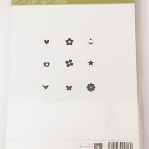 May include: A white card with the text "Itty Bitty Bits" and a set of nine small stamps featuring images of a heart, flower, cupcake, coffee cup, star, bird, butterfly, and two more flowers. The card also includes the text "Set of 9" and the company logo "Stampin' Up!"