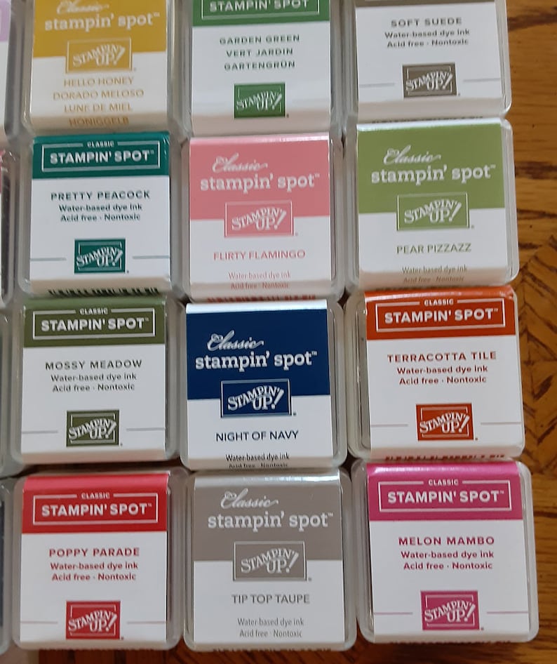 May include: A collection of 10 ink pads in various colors, including green, blue, red, pink, and brown. Each ink pad is labeled "Classic stampin' spot" and features a different color name, such as "Garden Green", "Night of Navy", and "Melon Mambo".