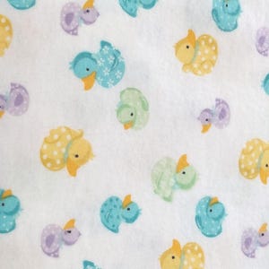 May include: White fabric with a repeating pattern of cartoon ducks in various colors. The ducks are in shades of yellow, blue, green, and purple, with orange beaks. Some ducks have polka dots or floral patterns.
