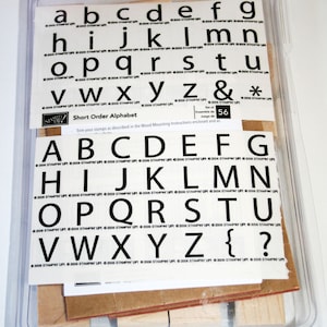 May include: A set of 56 alphabet letter stamps in a clear plastic case. The stamps are arranged in alphabetical order and are made of black rubber. The case is labeled "Short Order Alphabet" and includes instructions for mounting the stamps.