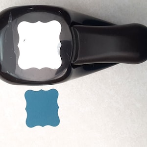 May include: A black paper punch with a white label and a teal blue paper punch out. The punch creates a square shape with rounded corners and decorative edges.