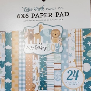 May include: A 6x6 inch paper pad by Echo Park Paper Co. featuring 24 double-sided papers. The cover displays a baby boy theme with animal illustrations and the text "our baby boy". The paper pad includes 65 lb. cardstock.