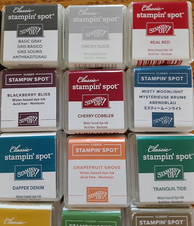 May include: Twelve ink pads in a grid pattern, each with a different color and name. The ink pads are labeled "Classic stampin' spot" and feature the words "STAMPIN' UP!" in a logo. The ink pad colors include Basic Gray, Smoky Slate, Real Red, Blackberry Bliss, Cherry Cobbler, Misty Moonlight, Dapper Denim, Grapefruit Grove, Tranquil Tide.