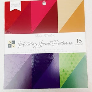 Könnte beinhalten: Eine Packung mit 18 doppelseitigen 15,24 cm x 15,24 cm großen Shimmer-Kartonbögen mit UV-Glanz. Die Packung enthält eine Vielzahl von Weihnachts-Juwel-Mustern in Rot, Rosa, Orange, Lila, Grün und Weiß.