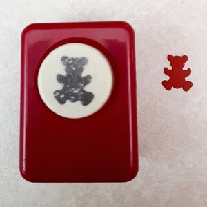 May include: Red plastic bear punch with a white circle showing a gray bear silhouette. A red paper bear cutout is next to the punch.