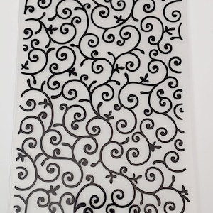 Puede incluir: Hoja de plástico transparente con un diseño en blanco y negro de enredaderas en espiral. El diseño se repite en toda la hoja.