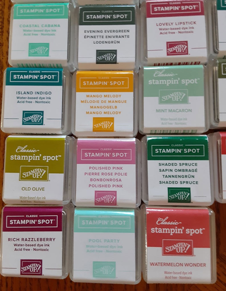 May include: A collection of 12 Stampin' Spot ink pads in various colors, including Coastal Cabana, Evening Evergreen, Lovely Lipstick, Island Indigo, Mango Melody, Mint Macaron, Old Olive, Polished Pink, Shaded Spruce, Rich Razzleberry, Pool Party, and Watermelon Wonder. Each ink pad is labeled with the color name and "Classic Stampin' Spot" in a white box with a green logo.