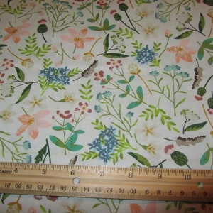 May include: White fabric with a repeating pattern of pink, blue, and green flowers. A wooden ruler with the text "FISKARS" is placed at the bottom of the image.