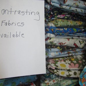 May include: A stack of colorful fabric scraps with a handwritten sign that reads "Contrasting Fabrics Available".