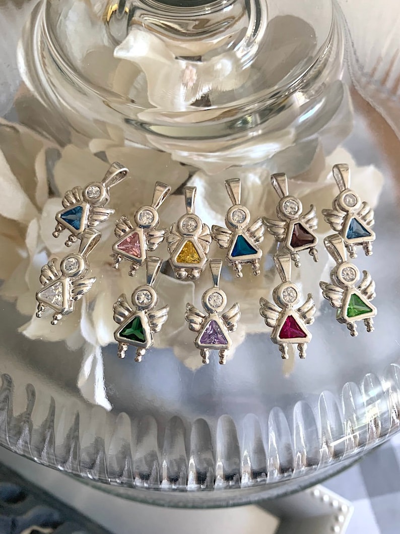 May include: A collection of silver angel charms with different colored gemstones. The charms feature a small angel with wings and a gemstone in the center. The gemstones are pink, yellow, blue, purple, green, and red.