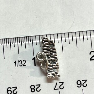 May include: Silver charm with the words "Happy Birthday" engraved on it. The charm is about 1 inch long and has a loop for attaching to a bracelet or necklace.