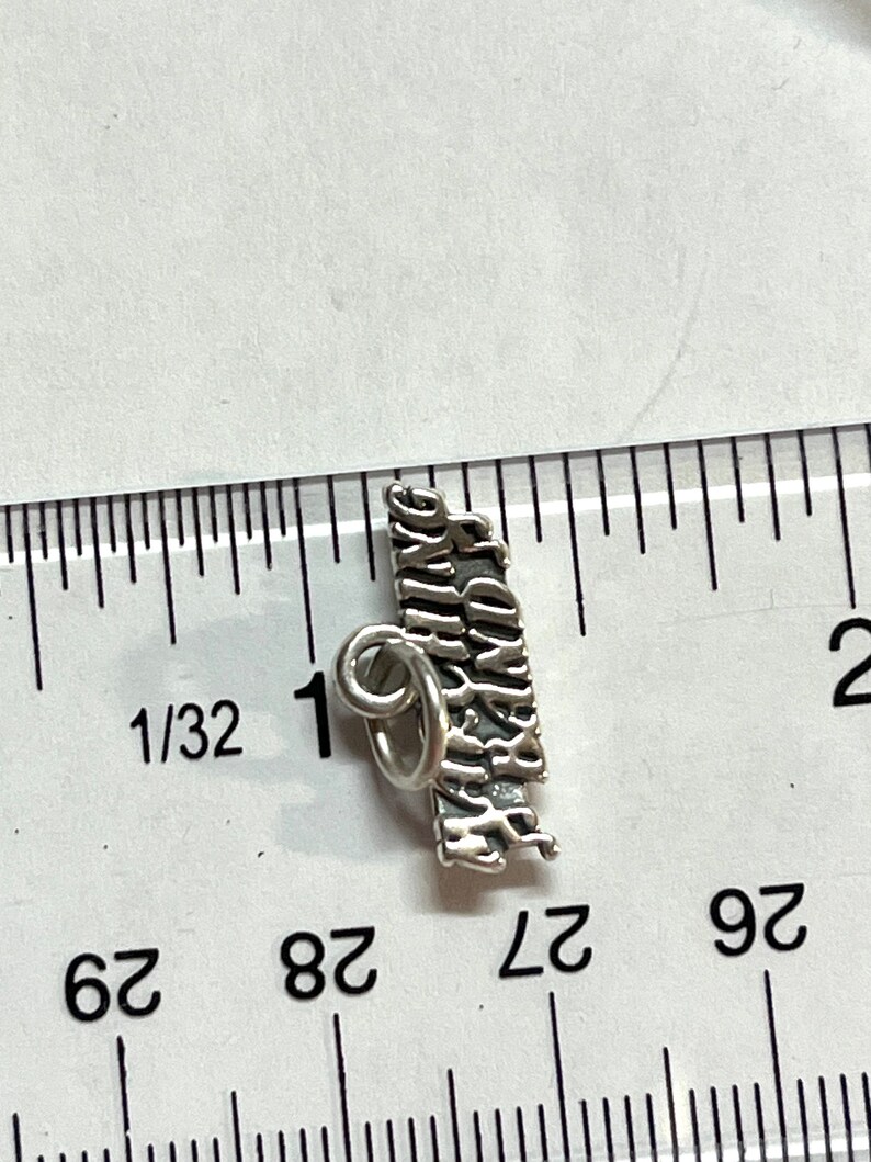 May include: Silver charm with the words "Happy Birthday" engraved on it. The charm is about 1 inch long and has a loop for attaching to a bracelet or necklace.