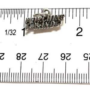 May include: Silver charm with the words "Marching Band" and a musical note. The charm is about 1 inch long and is measured against a ruler.