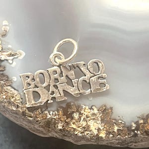 May include: Silver charm with the words "Born to Dance" in a stylized font.